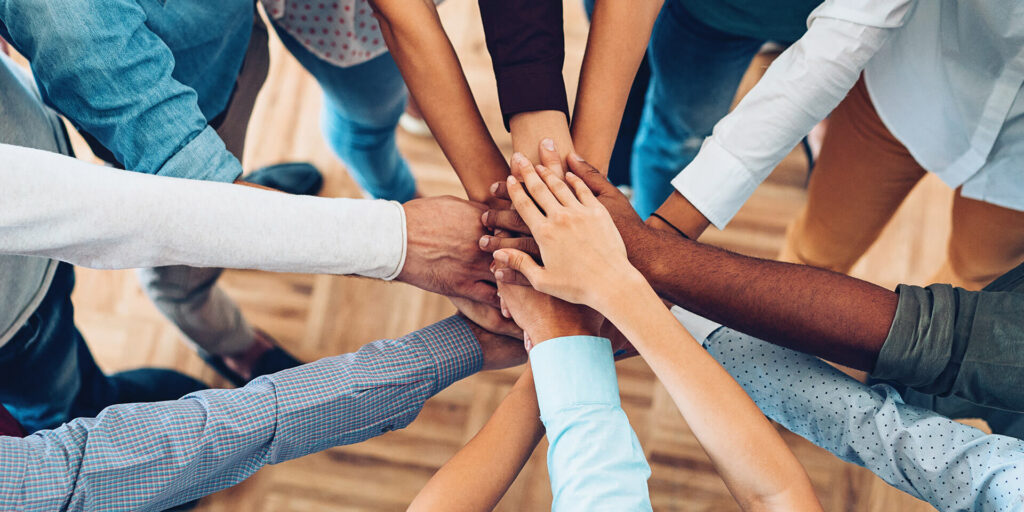 Aufeinander gelegte Hände einer Gruppe von Menschen mit verschiedenen Hautfarben